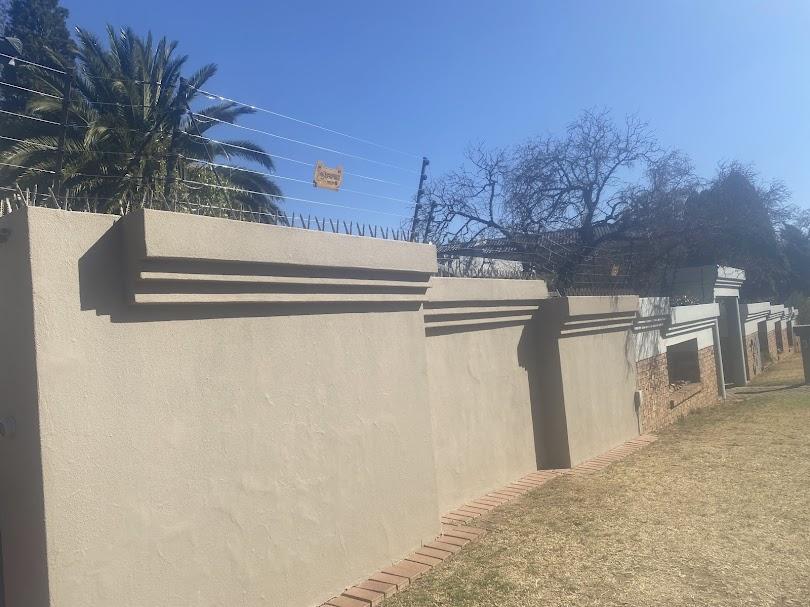 Multi-strand electric fence running along a long boundary wall in Alberton